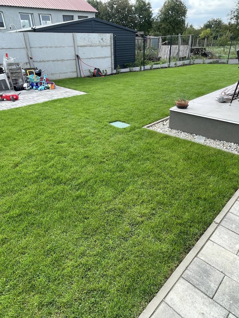 Finished, even lawn with a terrace and paving, and the irrigation valve box lid set into the grass