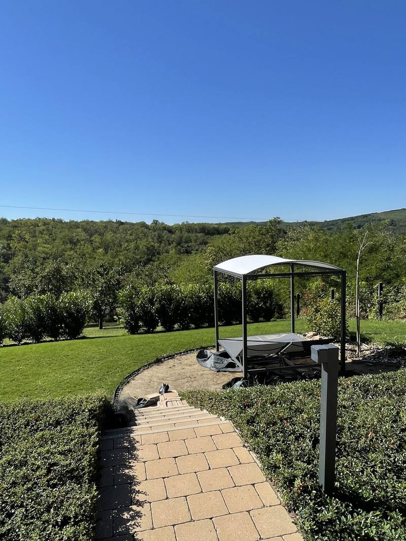 Paved garden path framed by clipped hedging, with a pergola and a long view behind it